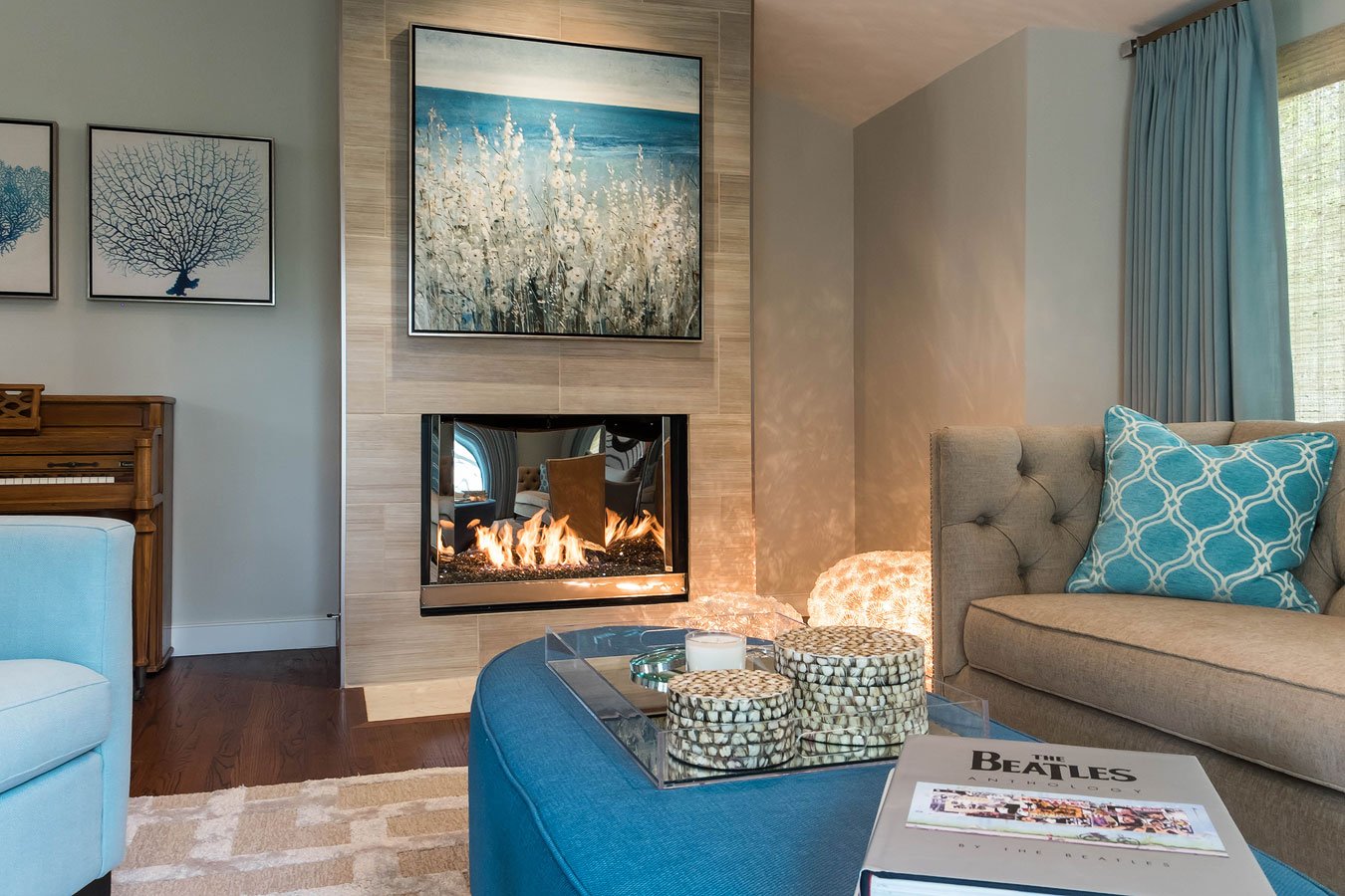 A freshly remodeled luxury living room with tufted sofa, linen drapery, coastal art and porcelain fireplace.